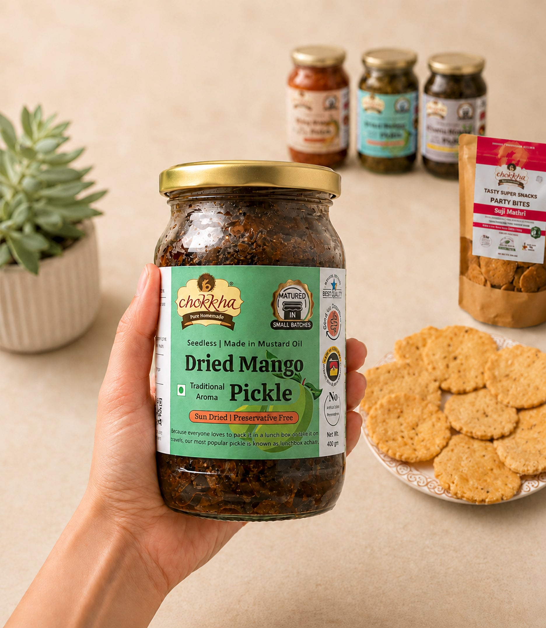 Hand holding a Chokkha Dried Mango Pickle jar beside mathri